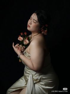 a woman in a white dress holding flowers and looking at the camera with her eyes closed