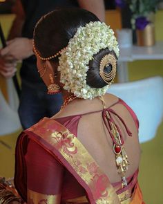 a woman wearing a red and gold saree with flowers in her hair is seen from the back