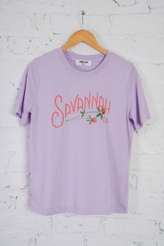 Get ready to show some local love with the Savannah Tee! This basic tee features a super soft, loose fit and a playful motif of flowers and wording that says "Savannah GA". Perfect for commemorating your visit here, this tee also boasts short sleeves, a round neckline, and a vibrant lilac color. Don't miss out on this unique tee! Brand- Double Zero Spring Purple T-shirt With Graphic Print, Purple Pre-shrunk T-shirt For Spring, Purple Graphic Print T-shirt For Spring, Double Zero, Basic Shorts, Lilac Color, Savannah Ga, Basic Tee, New Arrival Dress