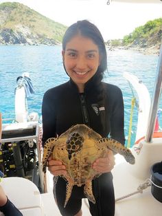 a woman holding a turtle in her hands on a boat