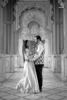 a man and woman standing together in front of a building with columns, pillars and arches