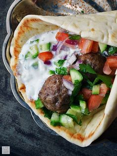 two pita breads filled with meatballs, vegetables and yogurt sauce