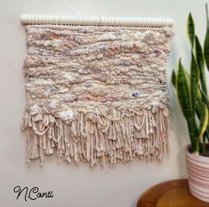 the wall hanging is made out of yarn and has fringes on it, along with a potted plant