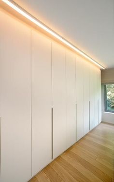 an empty room with white cupboards and wood flooring in front of a window