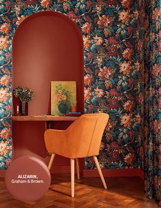 a wooden chair sitting in front of a red wall with flowers on it and a painting