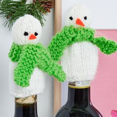 two crocheted snowmen holding hands on top of wine bottles next to a christmas tree