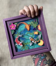 a person holding up a painting with fish and flowers on it