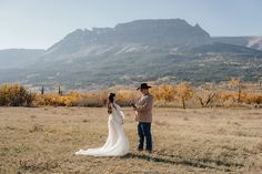 a bride and groom standing in an open field with mountains in the background at their wedding