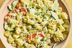 a bowl filled with macaroni salad on top of a wooden table next to a fork