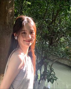 a woman standing next to a tree with her hair in the air and smiling at the camera