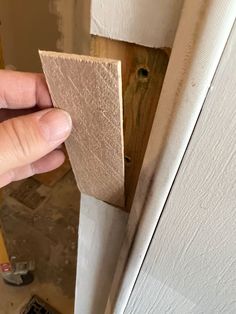 a person holding a piece of wood in their hand near a door with the bottom panel missing