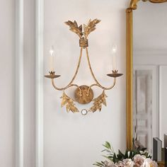 a gold wall light hanging on the side of a white wall next to a vase with flowers