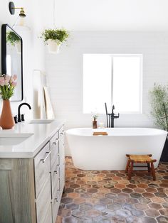 a white bath tub sitting in a bathroom next to a sink and window with potted plants