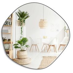 an oval mirror reflecting a dining room table and chairs with plants in the corner,