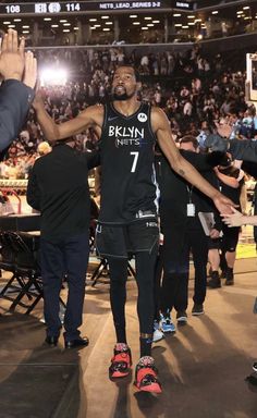 the basketball player is walking down the court with his hands in the air and people standing around him