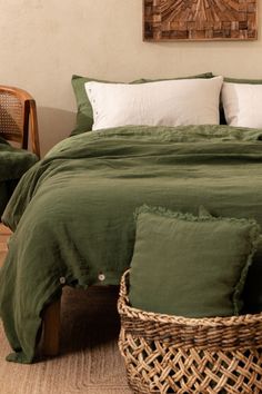 a bed with green linens and pillows in a small room next to a wicker basket