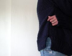 a woman in jeans and a sweater is holding her hand on her hip while standing against a white wall