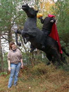 a woman standing next to a statue of a black horse and a man in a red cape