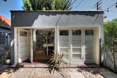 a small house with two doors open on the outside, and a potted plant in front of it