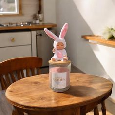 a small doll sitting on top of a table next to a jar with a bunny in it