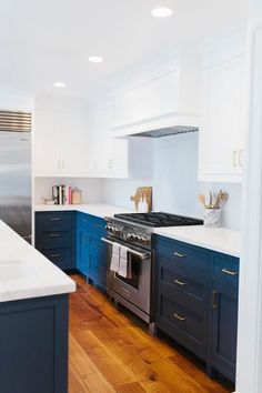 a kitchen with white and blue cabinets, wood flooring and stainless steel stove top oven