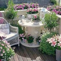 an outdoor patio with potted plants and flowers on the table in front of two wicker chairs