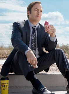 a man in a suit and tie sitting on a cement bench holding a small object