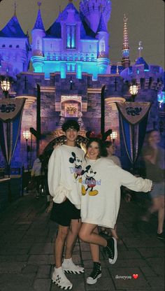 two people pose for a photo in front of the castle at disneyland world with their arms around each other