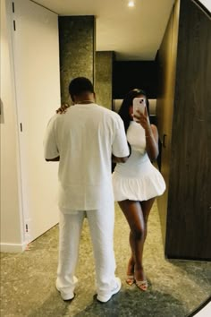 a man taking a photo of a woman in a white dress with her cell phone