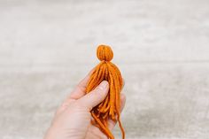 a hand holding an orange piece of yarn