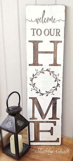 a wooden sign that says welcome to our home next to a lantern on a table