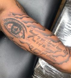 a man's arm with an all seeing eye tattoo on it and some clouds in the background