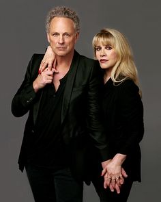 two people standing next to each other in front of a gray background with one person holding the other's hand