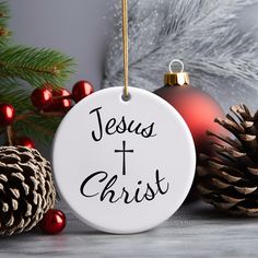 a white ornament with the words jesus and christ on it next to pine cones