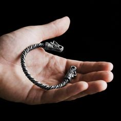 a hand holding a silver bracelet with two skulls on it