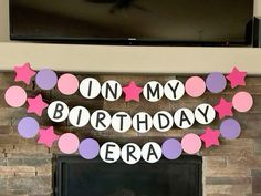 a birthday banner with pink, purple and white stars hanging on a fireplace mantel