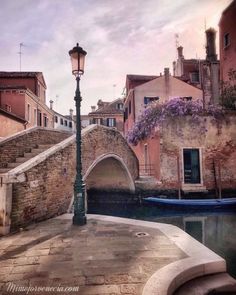 a lamp post sitting on the side of a river next to a bridge and buildings