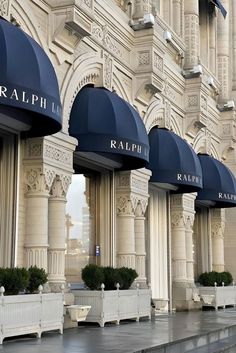 the exterior of a building with blue awnings and white planters in front