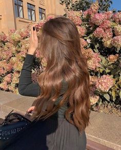 a woman sitting on a bench taking pictures with her cell phone in front of flowers