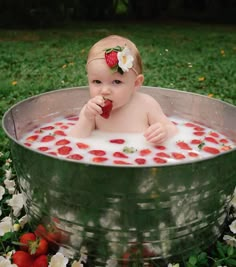 a baby sitting in a metal tub with strawberries