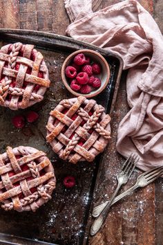 three raspberry pies on a baking sheet with fresh raspberries in the middle