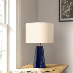 a blue table lamp sitting on top of a wooden table next to a white shade