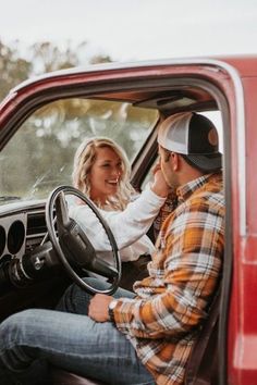 a man and woman sitting in the driver's seat of a red truck