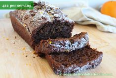 a loaf of chocolate cake sitting on top of a wooden cutting board next to an orange