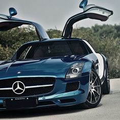 a blue mercedes sports car parked on the side of the road with its doors open