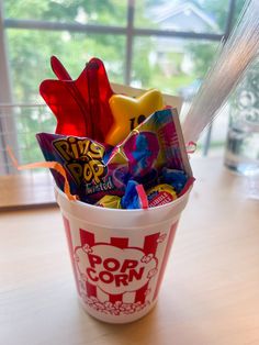 a cup filled with candy and candies on top of a wooden table next to a window