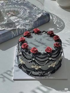 a black and white cake with red roses on it sitting on a table next to a book