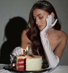 a woman in white gloves holding a cake with a lit candle on top of it