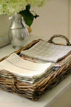 a wicker basket with folded napkins and flowers in the background on a counter