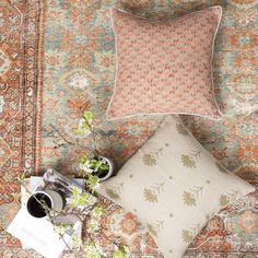 two pillows and a camera on a rug with flowers in vases next to them